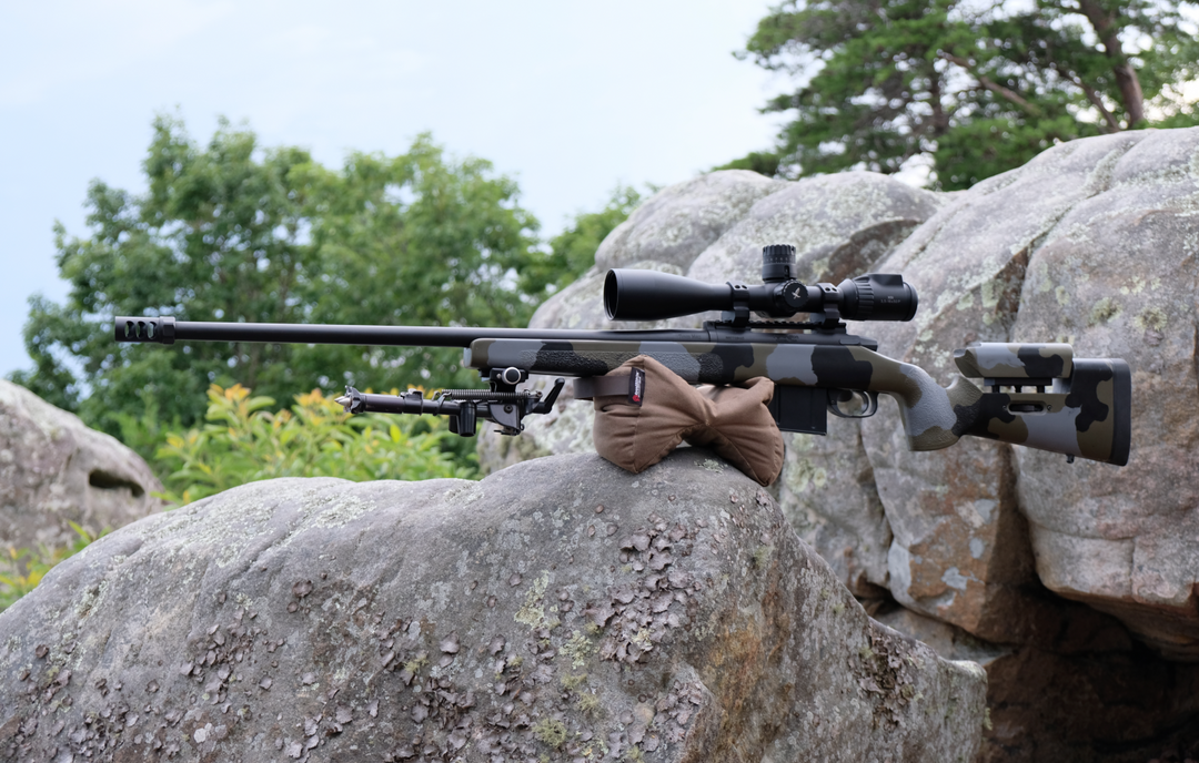 Armageddon Gear Pint Sized Gamechanger™ with Pigg River Logo holding up a precision rifle on a rock. - Sharps Mountain - SharpsMountain.com
