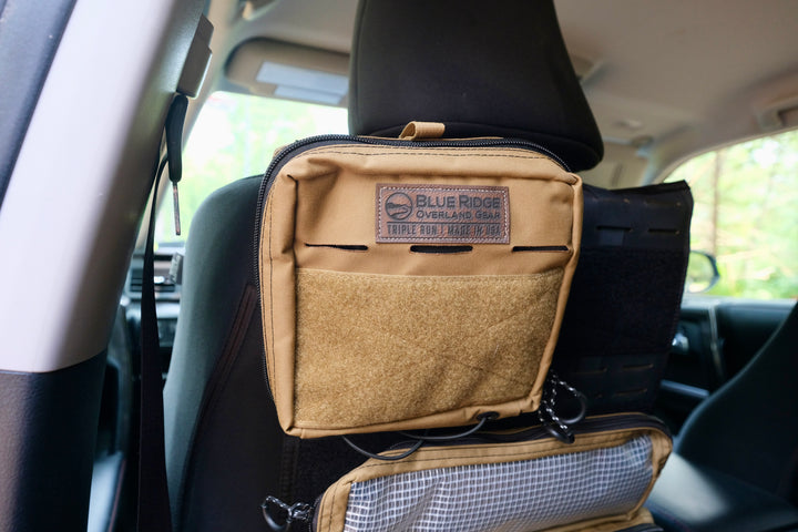 A black vehicle seat organizer pouch hanging from a car headrest, with a visible Blue Ridge Overland Gear logo patch on the front pocket.