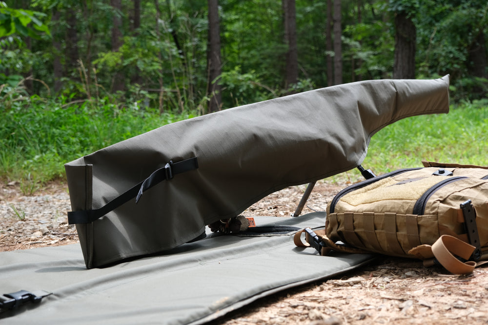 Suppressor Ready Rifle Cover protecting a precision rifle on a shooting mat in a wooded outdoor setting.